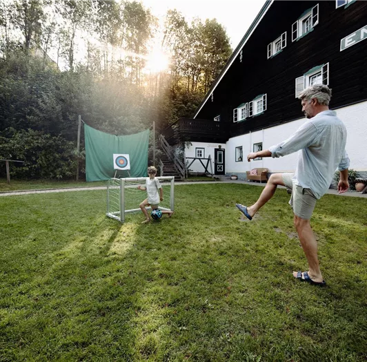 A man and a child are playing in the garden of the Resl Resort. In the background, the Ennshof.