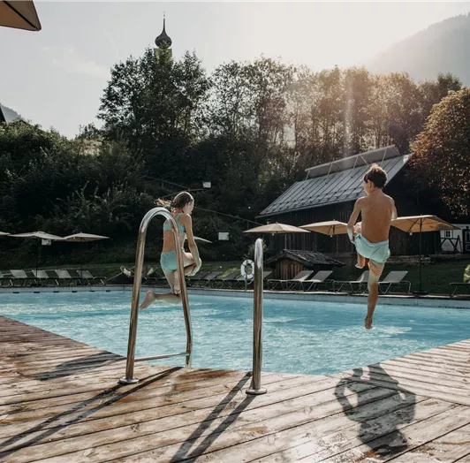 Two children are happily jumping in the Resl pool. The sun is shining, surrounded by green nature and cozy loungers.