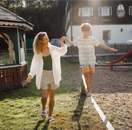 A woman and a boy are balancing on the slackline in the Resl garden.