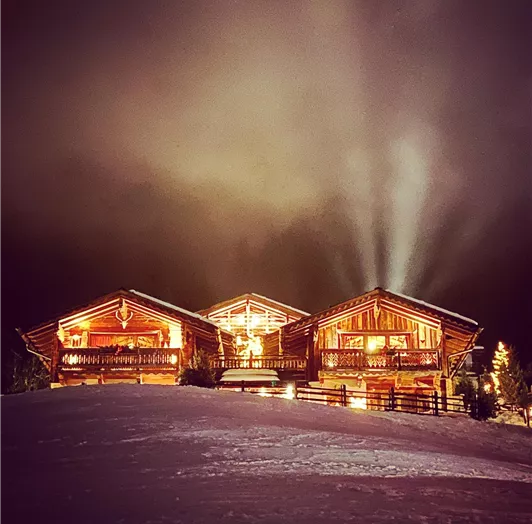 Magische Winterstimmung im Almdorf bei Nacht. Ein Anblick wie aus dem Bilderbuch: Warm erleuchtet liegen die urigen Chalets des Almdorfs eingebettet in die verschneite Landschaft. Das Licht strahlt einladend durch Fenster und Balkone, während mystische Nebelschwaden am Himmel für eine ganz besondere Atmosphäre sorgen. In dieser winterlichen Abendkulisse trifft alpine Gemütlichkeit auf magische Ruhe – ein unvergesslicher Moment für alle, die hier zu Gast sind.