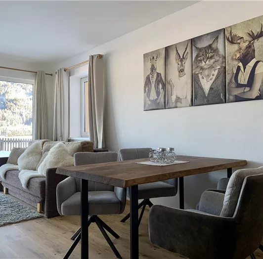 Gemütliches Wohnerlebnis mit alpinem Flair. Der stilvoll eingerichtete Wohnbereich unseres Appartements vereint modernes Design mit rustikalem Charme. Große Fensterfronten bieten einen atemberaubenden Blick auf die Berglandschaft und sorgen für viel Tageslicht. Die bequeme Couch lädt zum Entspannen ein, während der großzügige Esstisch aus Massivholz genügend Platz für gesellige Abende bietet. Hochwertige Polstermöbel und warme Holzböden runden das behagliche Ambiente ab – ideal für erholsame Tag