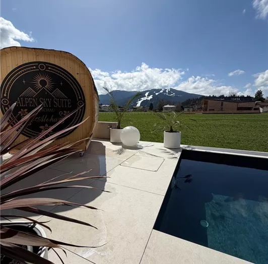 Eine moderne Terrasse mit einem Swimmingpool, Sauna und Blick auf die Berge. Die klare Aussicht und die sonnige Atmosphäre schaffen eine entspannende Stimmung.