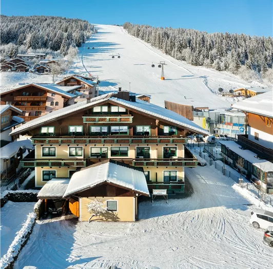 Ein gemütliches Hotel im Schnee mit einer Skipiste im Hintergrund.