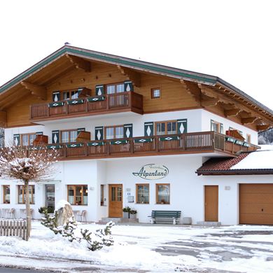 Ein charmantes Gästehaus im alpenländischen Stil, umgeben von Schnee. Die Fassade ist hell und einladend, mit vielen Fenstern und Balkonen.