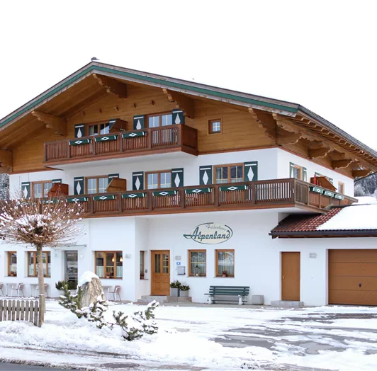 Ein charmantes Gästehaus im alpenländischen Stil, umgeben von Schnee. Die Fassade ist hell und einladend, mit vielen Fenstern und Balkonen.
