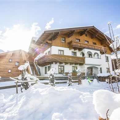 Ein schönes Haus im Schnee mit einem großen Balkon. Die Landschaft ist winterlich und sonnig.