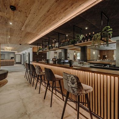 Die moderne Bar im Resl Resort mit Holzdekor und stilvollen Sitzgelegenheiten. Die sanfte Beleuchtung schafft eine einladende Atmosphäre.