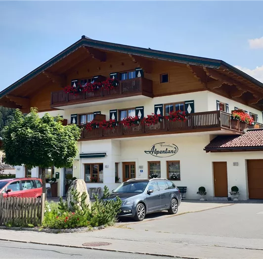 Ein traditionelles Gebäude in einer ländlichen Umgebung. Es hat mehrere Balkone mit Blumen und eine gepflegte Landschaft.