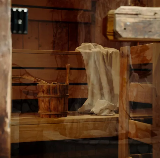 A wooden-clad sauna with a bench, a bucket, and a towel. Lean back and enjoy your sauna session.