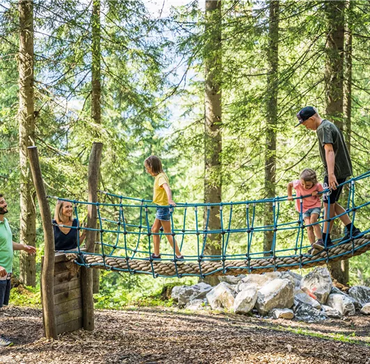 Eine Familie spielt auf einer Wackelbrücke im Wald.