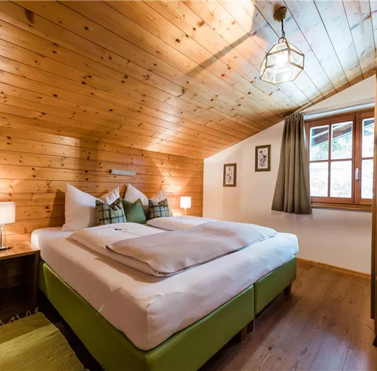 Ein gemütliches Schlafzimmer mit holzverkleideten Wänden und einem großen Bett. Das Zimmer hat ein Fenster mit Blick nach draußen und eine warme, einladende Atmosphäre.