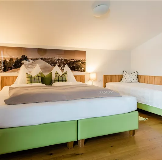 Ein gemütliches Schlafzimmer mit einem großen Bett und einem zusätzlichen Einzelbett. Die Wände sind hell dekoriert, und es gibt sanfte Beleuchtung von den Nachttischen.