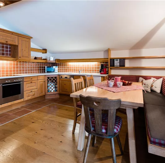 Eine gemütliche Küche mit Holzschränken und einer Essecke. Das Licht ist hell, und die Einrichtung vermittelt eine einladende Atmosphäre.