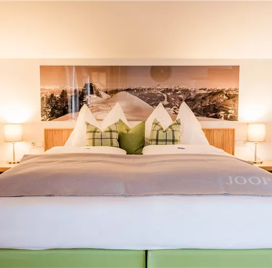 Ein modernes Hotelzimmer mit einem großen Bett und einer ansprechenden Wanddekoration. Der Raum ist hell und einladend, mit sanften Farben und gemütlicher Beleuchtung.