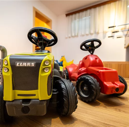 Zwei Spielzeugtraktoren stehen auf einem Holzboden. Der grüne Traktor ist von der Marke Claas, und neben ihm steht ein roter Traktor.