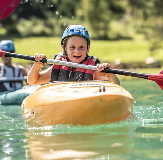 Ein fröhlicher Junge paddelt in einem gelben Kajak auf klarem Wasser.