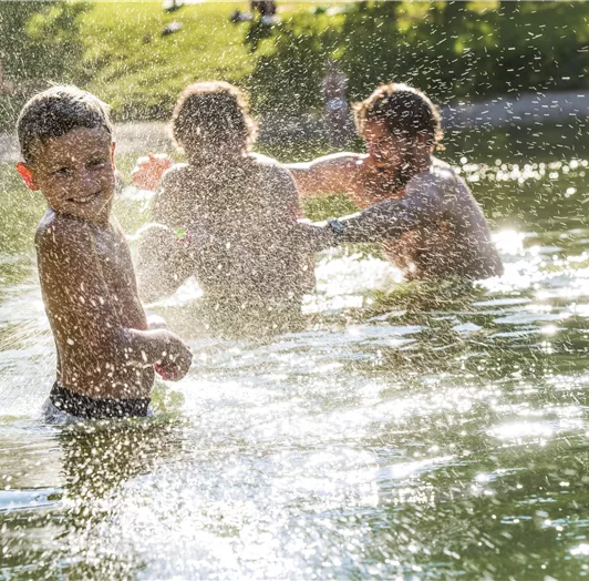 Ein fröhlicher Junge spielt im Wasser mit zwei anderen Kindern.