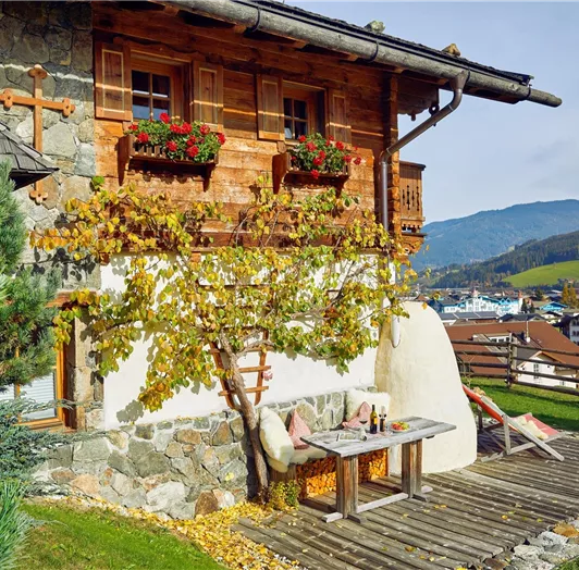 Romantische Sonnenterrasse mit Panoramablick. Diese charmante Terrasse ist ein echter Rückzugsort für Genießer. Umrahmt von Naturstein und Holz lädt die gemütliche Sitzecke mit gemauerter Rückenlehne und weichen Polstern zum Verweilen ein. Liegestühle mit Blick über das Tal und die umliegenden Berge sorgen für entspannte Momente in der Sonne. Ideal für ein Frühstück im Freien oder ein Glas Wein bei untergehender Sonne – mit traumhafter Aussicht inklusive.