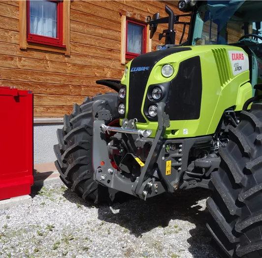 Ein grüner Traktor mit großen Reifen steht vor einem Holzgebäude.