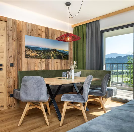 Ein modernes Esszimmer mit einem großen Tisch und gestuften Stühlen. Die große Fensterfront bietet einen Blick auf die umliegende Natur und die Berge. Dachsteinblick