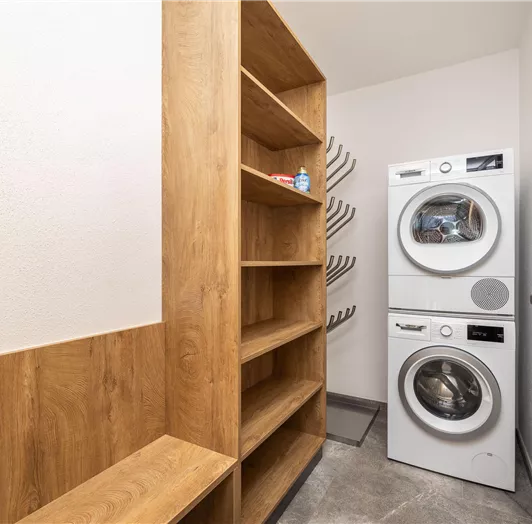Ein praktischer Hauswirtschaftsraum mit Waschmaschine und Trockner. Regale aus Holz bieten zusätzlichen Stauraum.