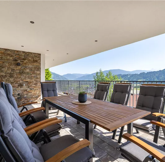 Eine großzügige Terrasse mit einem großen Holztisch und bequemen Stühlen.