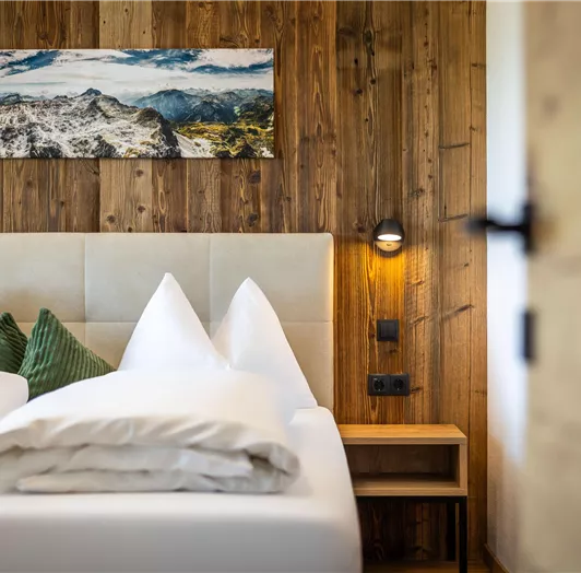 Ein gemütliches Schlafzimmer mit einem Holzinterieur und einem großen Bild an der Wand. Mit Aussicht auf die Natur und Berge.