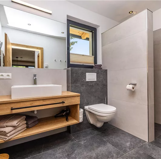 Ein modernes Badezimmer mit einem rechteckigen Waschbecken und Holzmöbeln. Die Wände sind grau gefliest und es gibt ein Fenster mit Blick nach draußen.