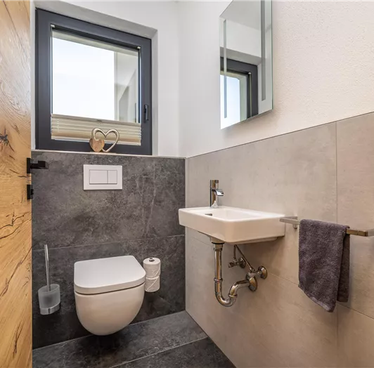 Im Appartement TYP B befindet sich ein separates modernes Badezimmer mit Toilette und einem kleinen Waschbecken. Es gibt einen großen Spiegel und ein Fenster, das Tageslicht hereinlässt.