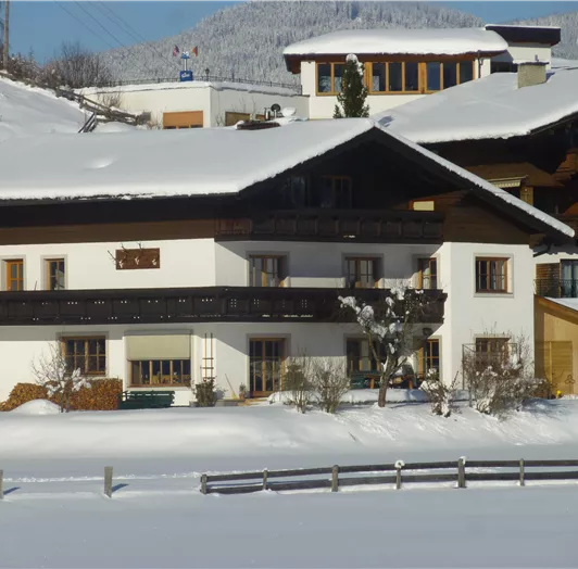Ein schönes Haus im Schnee mit typischer alpiner Architektur. Die Umgebung ist winterlich und friedlich, umgeben von Bergen.