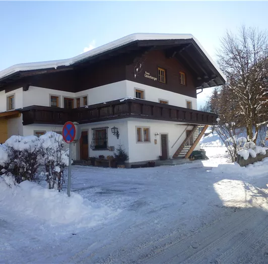 Ein gemütliches Haus im Alpenstil, umgeben von Schnee. Die Kälte des Winters ist deutlich sichtbar, und die Umgebung ist idyllisch.