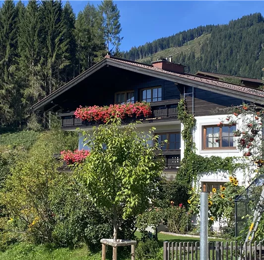 Ein charmantes Haus in den Bergen, umgeben von Bäumen und Blumen. Die Balkone sind mit bunten Pflanzen geschmückt.