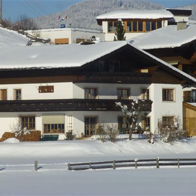 Ein schönes Haus im Schnee mit typischer alpiner Architektur. Die Umgebung ist winterlich und friedlich, umgeben von Bergen.