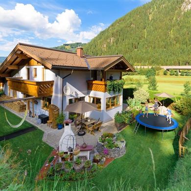 A beautiful house with a balcony, surrounded by green meadow and mountains.