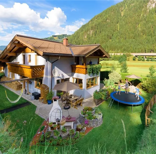 Ein schönes Haus mit Balkon, umgeben von grüner Wiese und Bergen.