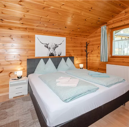 Ein gemütliches Schlafzimmer mit Holzwänden und einem großen Bett. Es gibt sanfte Farben und Fenster, die natürliches Licht hereinlassen.