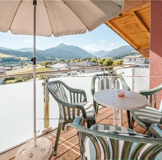 Eine gemütliche Terrasse mit einem Tisch und vier Stühlen. Im Hintergrund sind sanfte Hügel und Berge sichtbar.
