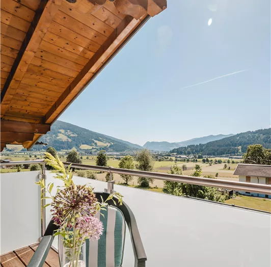 Ein Balkon mit Blick auf eine malerische Landschaft und sanfte Hügel. Ein Tisch mit einer Blume und einem Glas steht bereit für einen entspannten Moment.