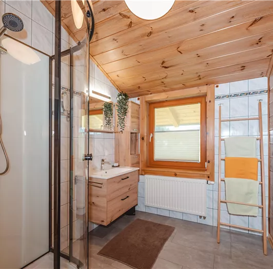 Ein modernes Badezimmer mit Holzverkleidung. Es verfügt über eine Dusche, ein Waschbecken und ein Fenster mit natürlichem Licht.