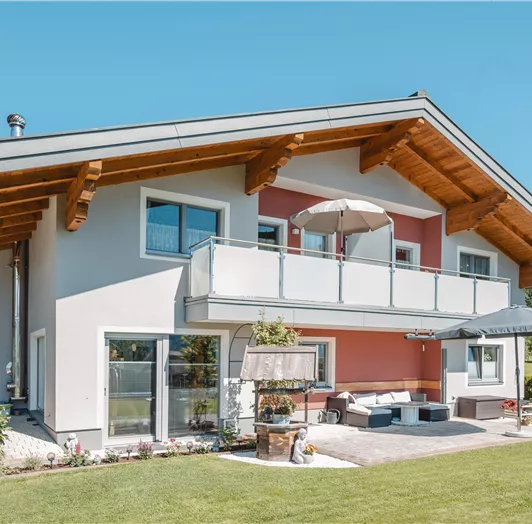 Ein modernes Haus mit einem großzügigen Balkon und schöner Umgebung. Der Garten ist gut gepflegt und bietet eine einladende Atmosphäre.