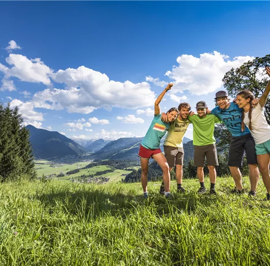 Eine Gruppe von Freunden steht fröhlich auf einer Wiese in den Bergen.