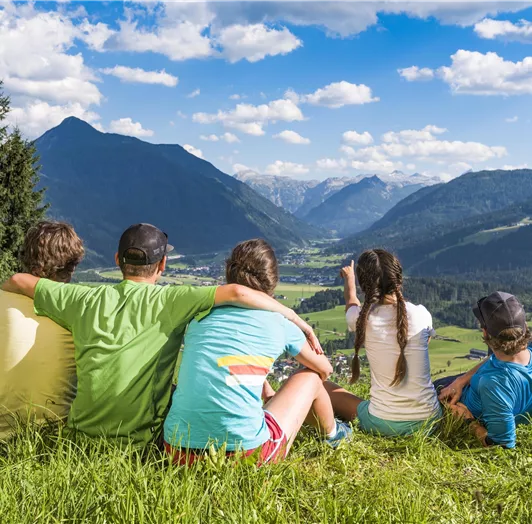 Eine Gruppe von Freunden sitzt auf einer Wiese und blickt auf die Berge.