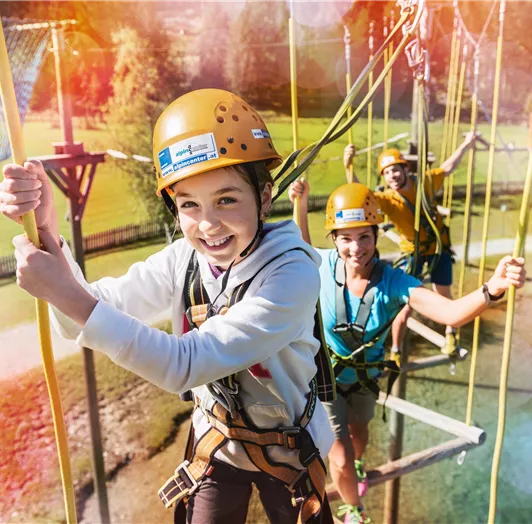 Eine Gruppe von Menschen in Sicherungsgeschirr, die an einem Kletterparcours teilnehmen.