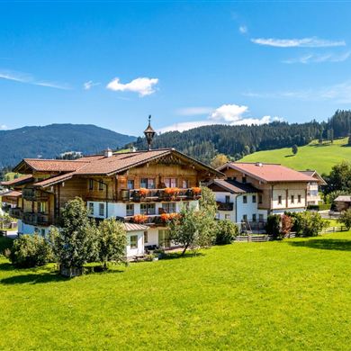 A picturesque farmhouse surrounded by green meadows and gentle hills. The bright blue sky adds a friendly atmosphere to the landscape.