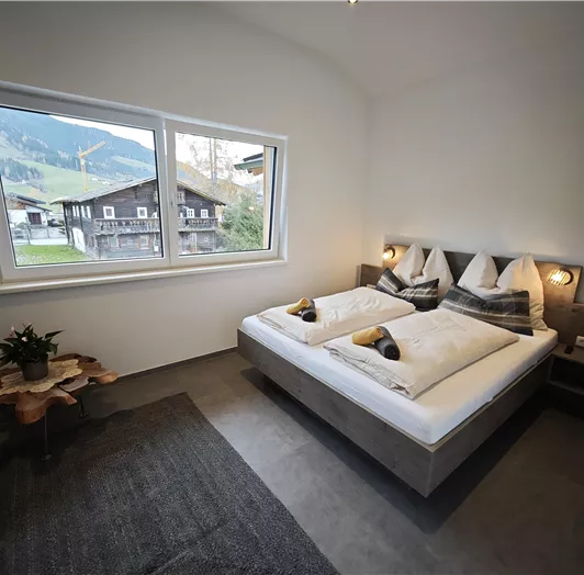 Ein gemütliches Schlafzimmer mit einem Doppelbett und großen Fenstern. Die Aussicht zeigt grüne Berge und traditionelle Gebäude.