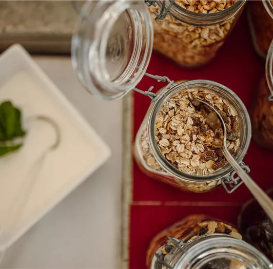 A selection of oatmeal in jars is on the buffet. Next to it is a bowl of yogurt with a mint leaf.