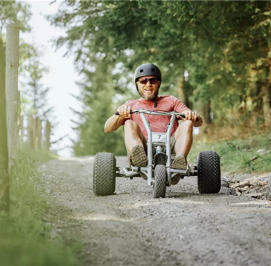 Hermann Maier fährt mit einem Go-Kart auf einem schmalen Waldweg.