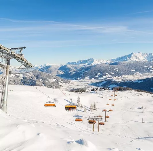 Ein schöner Blick auf eine schneebedeckte Landschaft mit Berggipfeln im Hintergrund. Eine Gondelbahn fährt über die winterliche Szenerie.