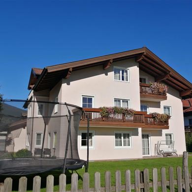 Ein zweigeschossiges Gebäude mit Balkonen und Blumen. Umgeben von grünen Wiesen und Bäumen.