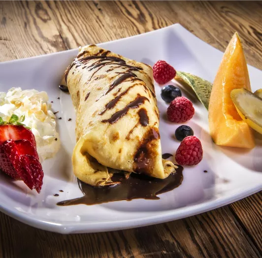 Ein köstlicher Eispalatschinke mit Schokoladensauce auf einem weißen Teller. Dazu frische Früchte und Sahne.